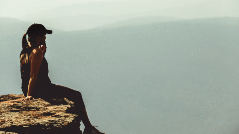 picture of woman sitting on the cliff ledge looking out at the view